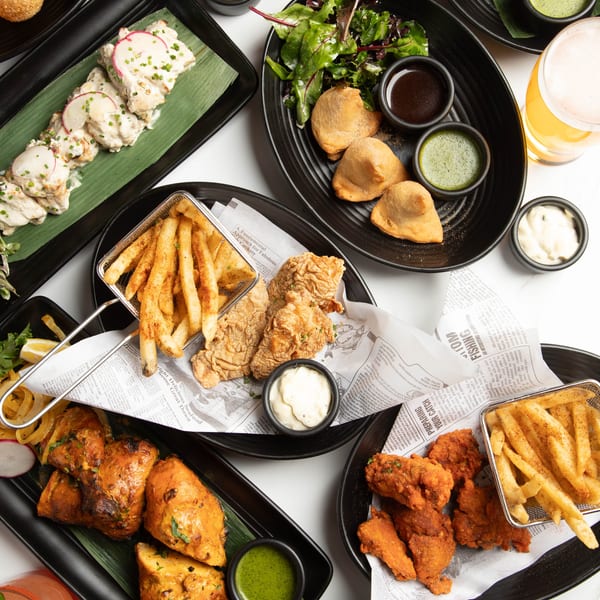 Overhead view of various Indian dishes including chicken, samosas, fries, and sauces on a white table.