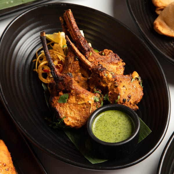 Grilled lamb chops with a side of green chutney and pickled onions on a black plate.