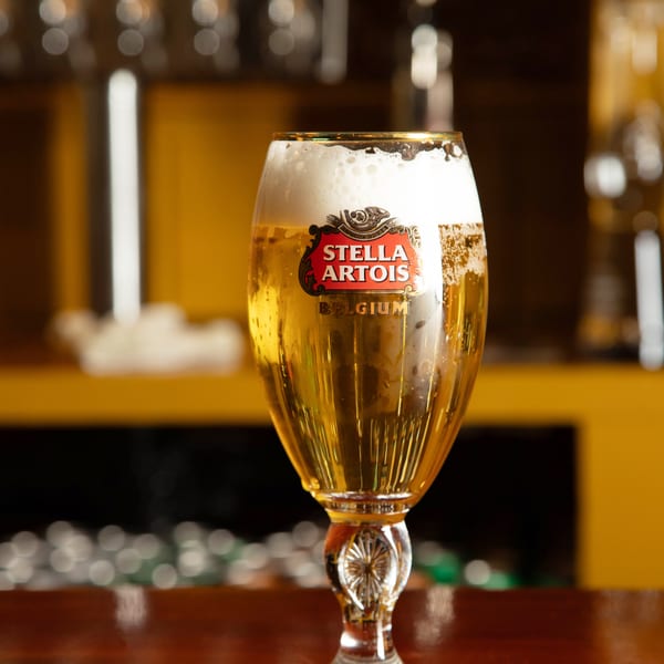 A Stella Artois beer glass filled with golden lager and foam sits on a dark wooden bar.
