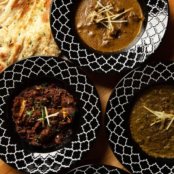 Overhead view of four Indian dishes in black patterned bowls and a side of naan bread.