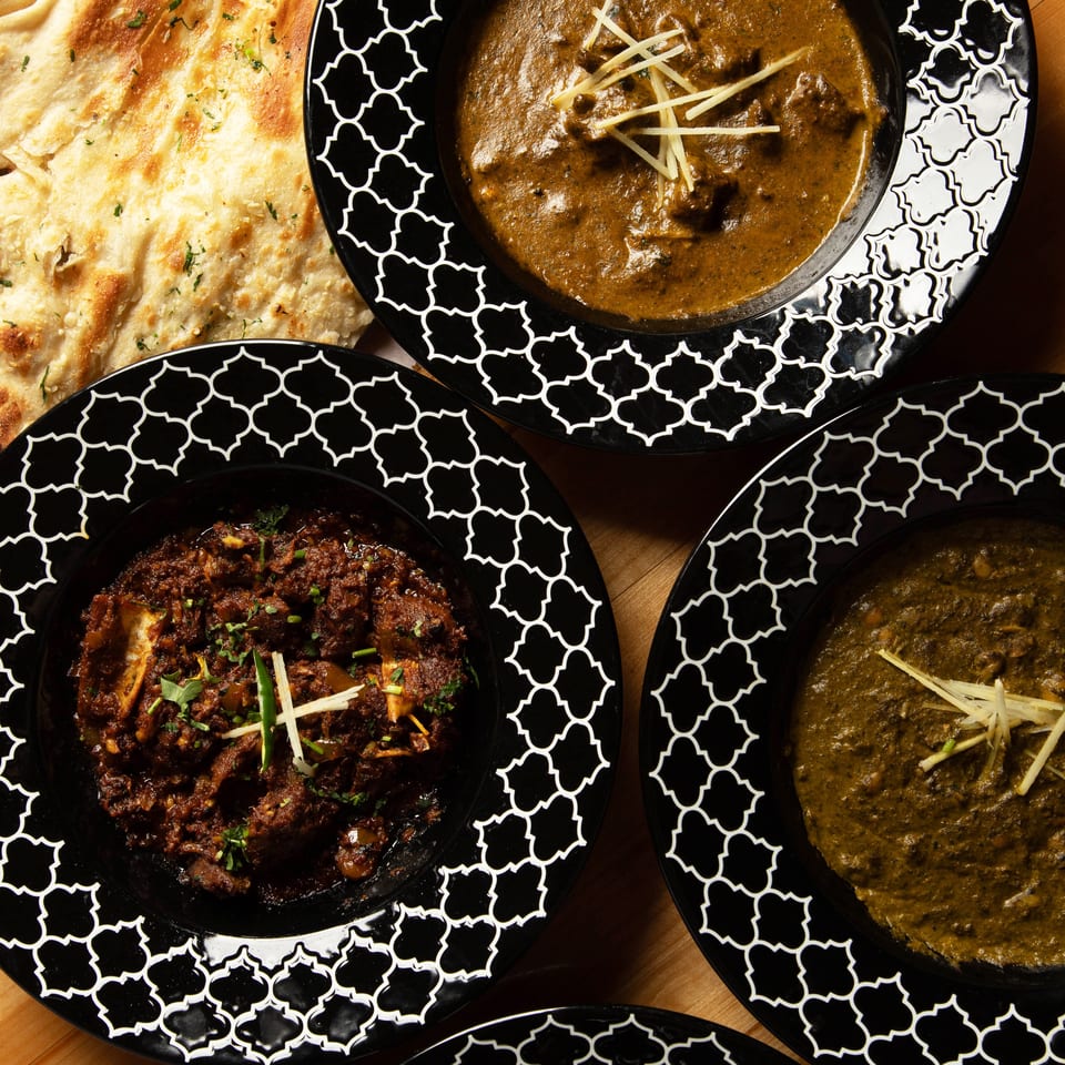 Overhead view of four Indian dishes in black patterned bowls and a side of naan bread.