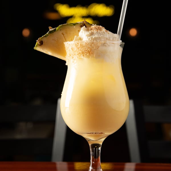 A creamy yellow pineapple cocktail with whipped cream, toasted coconut, and a pineapple wedge.