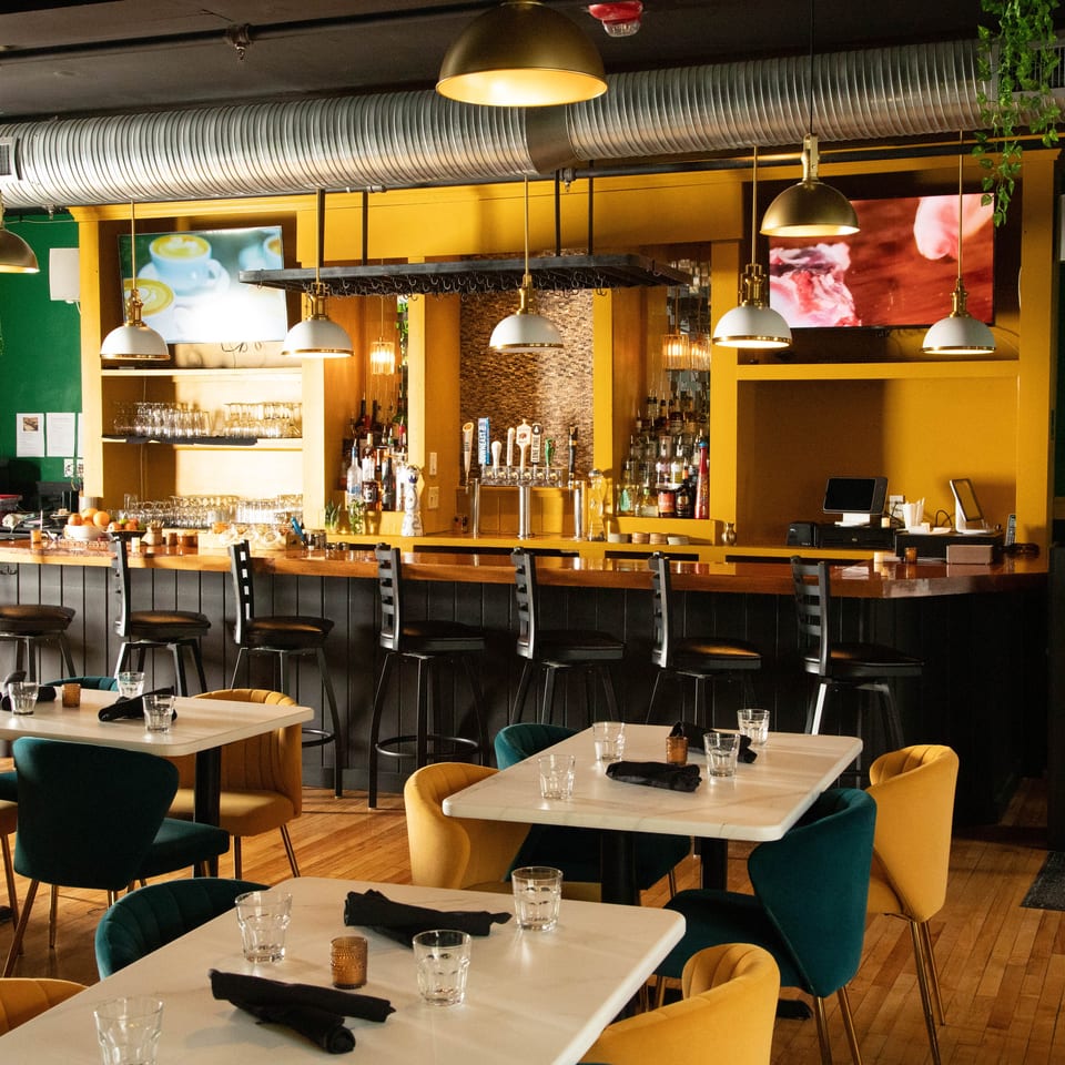 Bombay Bistro restaurant interior with a bar, dining tables, and yellow and green walls.