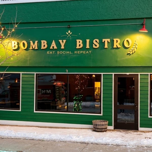 The Bombay Bistro restaurant exterior at dusk, with snow on the ground and a tree wrapped in lights.