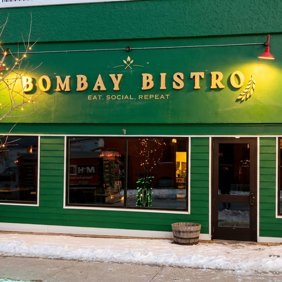 The Bombay Bistro restaurant exterior at dusk, with snow on the ground and a tree wrapped in lights.