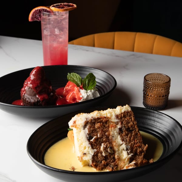 Two desserts, a chocolate lava cake and a slice of carrot cake, with a pink cocktail.