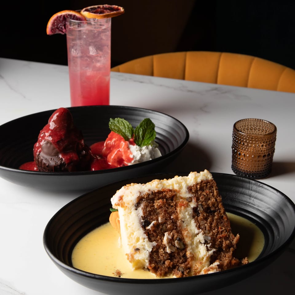 Two desserts, a chocolate lava cake and a slice of carrot cake, with a pink cocktail.