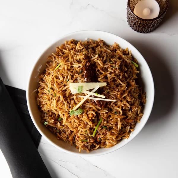 Overhead view of a bowl of spiced rice with ginger and cilantro, next to a candle.