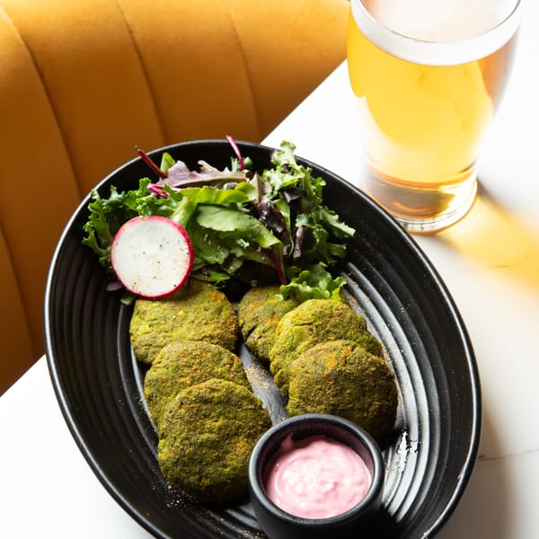 Green falafel patties with a side salad, pink sauce, and a glass of beer on a white table.
